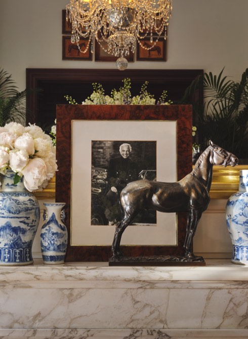 Porcelain vases, framed photographs, and metal horse on marble mantle.
