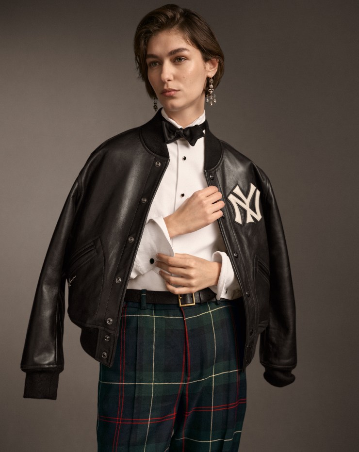 Woman wears black leather Yankees jacket, tuxedo shirt, and plaid pants.