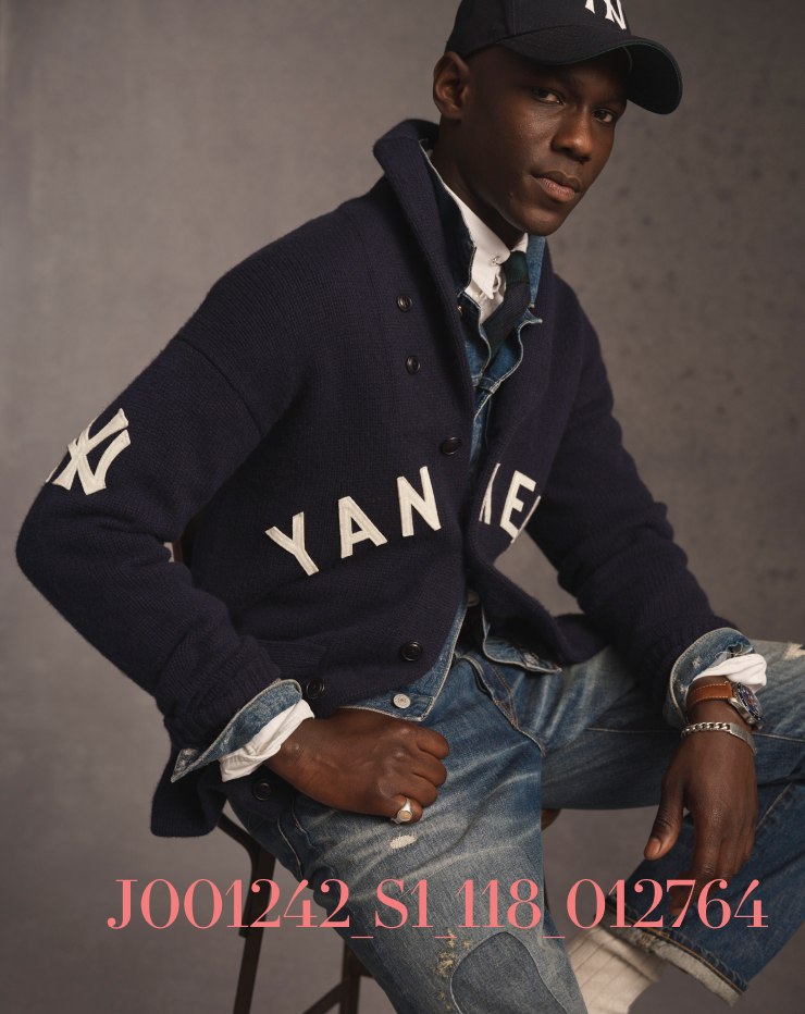 Man wears navy blue Yankees cardigan and ball cap.