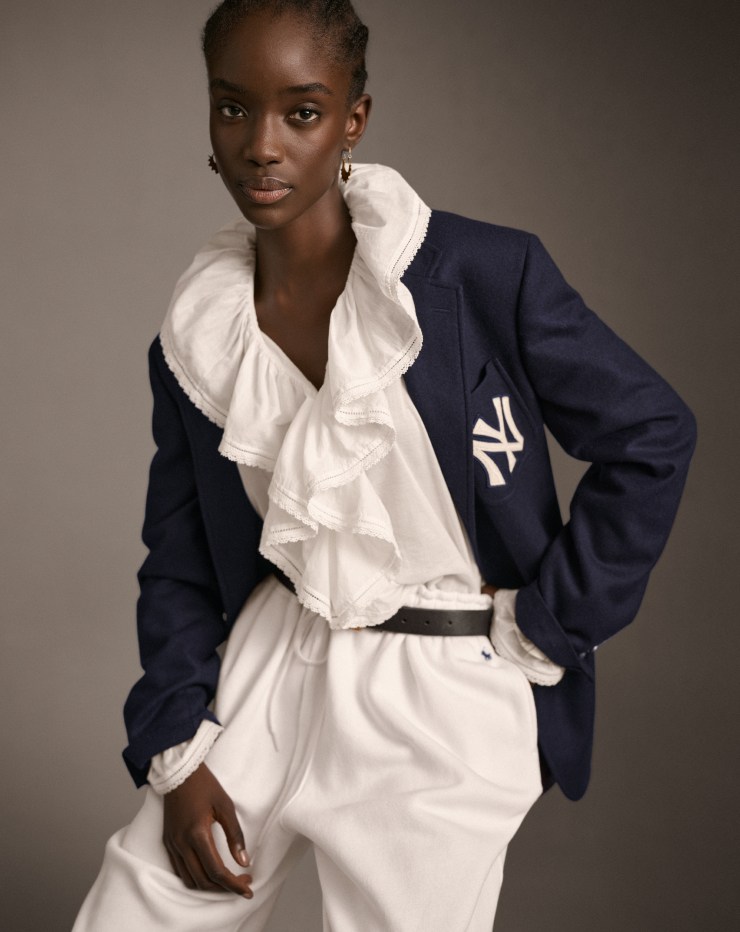 Woman wears navy blue Yankees blazer, white blouse, and white pants.